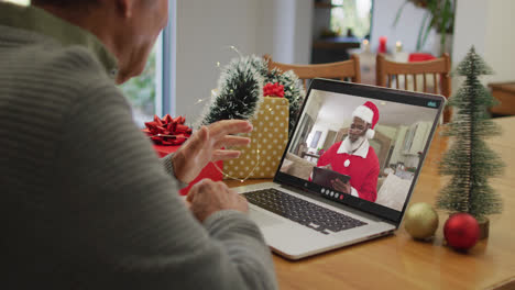 Caucasian-senior-man-having-christmas-video-call-on-laptop-with-african-american-santa-on-screen