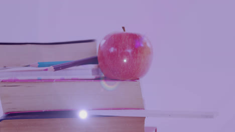Animation-of-glowing-light-over-apple-on-stack-of-books