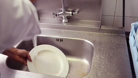 Kitchen-porter-cleaning-plates-in-sink