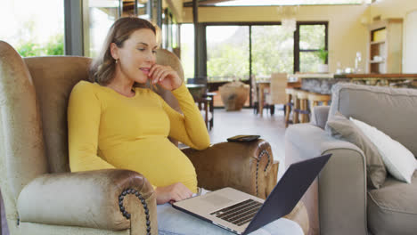 Glückliche-Kaukasische-Schwangere-Frau-Sitzt-Im-Sessel-Und-Benutzt-Laptop