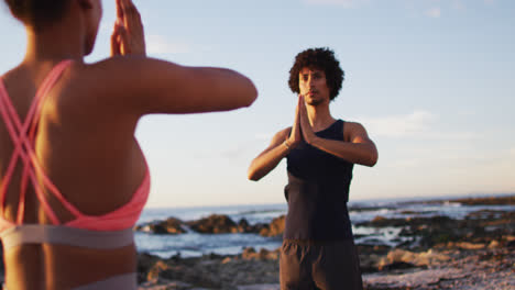 African-american-couple-practicing-yoga-together-on-the-rocks-near-the-sea