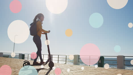 Animation-of-moving-spots-over-biracial-woman-riding-scooter-on-promenade