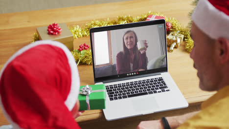 Caucasian-father-and-son-with-santa-hats-using-laptop-for-christmas-video-call-with-woman-on-screen
