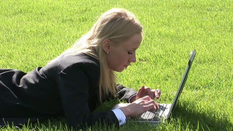 Mujer-Recostada-Sobre-El-Césped-Usando-Computadora-Portátil