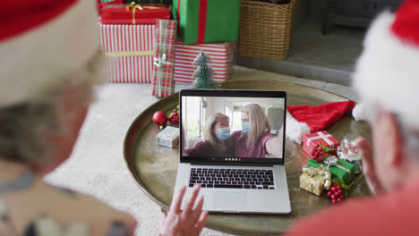 Caucasian-senior-couple-using-laptop-for-christmas-video-call-with-family-on-screen