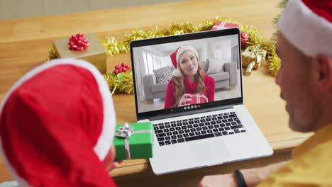 Caucasian-father-and-son-with-santa-hats-using-laptop-for-christmas-video-call-with-woman-on-screen