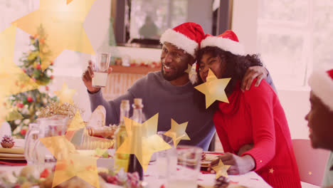 Animation-Von-Sternen,-Die-über-Eine-Glückliche-Afroamerikanische-Familie-Fallen,-Die-Weihnachtsmützen-Trägt-Und-Zu-Abend-Isst