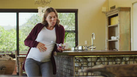Caucasian-pregnant-woman-sitting-in-kitchen-and-eating-ice-cream