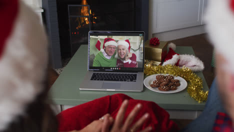 Caucasian-couple-on-laptop-video-call-with-senior-couple-at-christmas-time