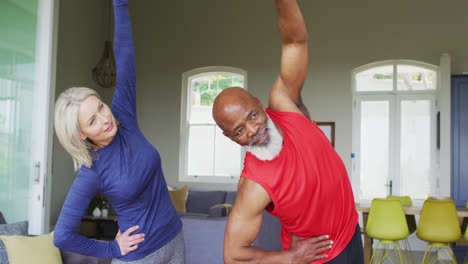 Mixed-race-senior-couple-performing-stretching-exercise-together-at-home
