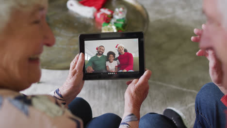 Senior-caucasian-couple-using-tablet-for-christmas-video-call-with-happy-family-on-screen