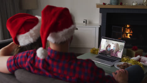 Caucasian-couple-on-laptop-video-call-with-family-in-face-masks-at-christmas-time