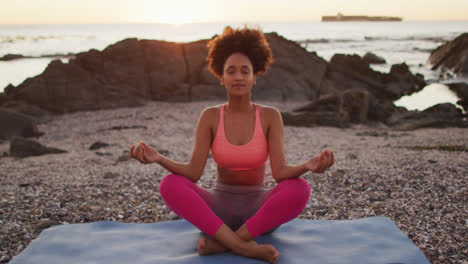 Mujer-Afroamericana-Practicando-Yoga-Y-Meditando-En-Las-Rocas-Cerca-Del-Mar-Durante-La-Puesta-De-Sol