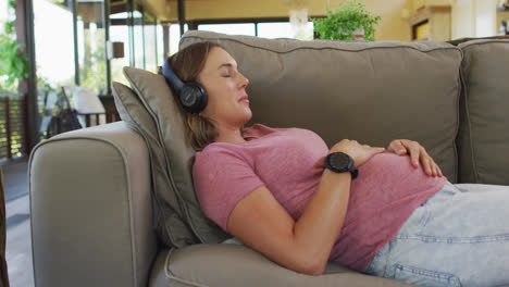 Relaxed-caucasian-pregnant-woman-lying-on-sofa-and-listening-to-music