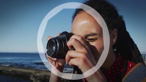Animation-of-circles-over-biracial-woman-taking-photo-with-camera-by-sea