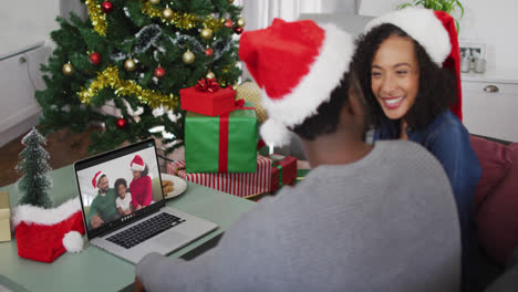 Una-Pareja-Afroamericana-Con-Gorros-De-Papá-Noel-Teniendo-Una-Videollamada-En-Una-Computadora-Portátil-En-Casa-Durante-La-Navidad
