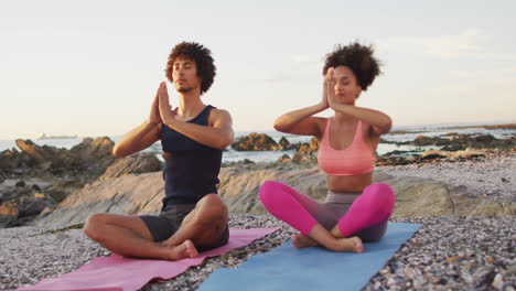 African-american-couple-practicing-yoga-and-meditating-together-on-the-rocks-near-the-sea