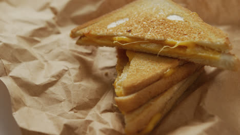 Video-of-close-up-of-toasted-cheese-sandwiches-on-brown-paper-over-grey-background