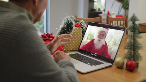Caucasian-senior-man-having-christmas-video-call-on-laptop-with-caucasian-santa-on-screen