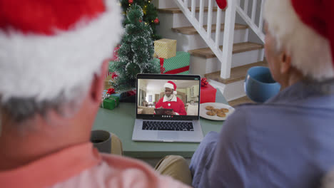 Happy-caucasian-senior-couple-on-laptop-video-call-with-santa-claus-at-christmas-time