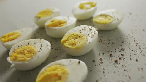Video-of-close-up-of-peppered-halves-of-hard-boiled-eggs-on-grey-background