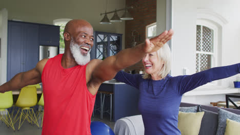 Mixed-race-senior-couple-performing-stretching-exercise-together-at-home