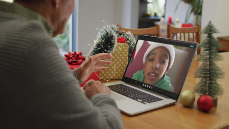 Caucasian-senior-man-having-christmas-video-call-on-laptop-with-african-american-boy-on-screen