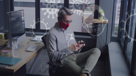 Animation-of-virus-icons-over-caucasian-businessman-with-face-mask-talking-on-smartphone-in-office