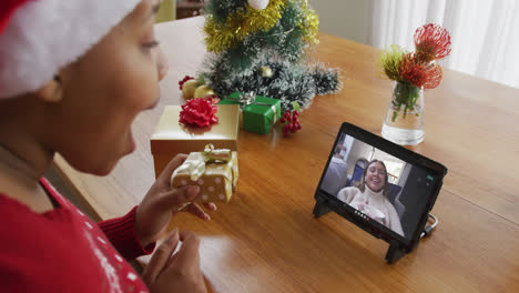 Afroamerikanische-Frau-Mit-Weihnachtsmütze-Nutzt-Tablet-Für-Weihnachtsvideoanruf-Mit-Frau-Auf-Dem-Bildschirm
