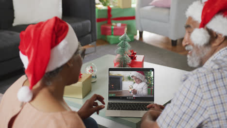 Glückliches-Afroamerikanisches-Seniorenpaar-Beim-Laptop-Videoanruf-Mit-Junge-In-Weihnachtsmütze-Zur-Weihnachtszeit