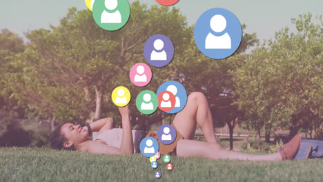 Animation-of-media-icons-over-biracial-woman-using-smartphone-in-park