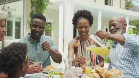 Glückliche-Afroamerikanische-Familie-Trinkt-Saft-Und-Frühstückt-Im-Garten