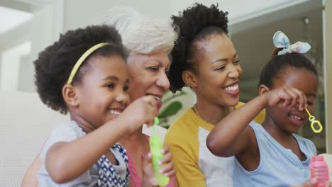 Glückliche-Afroamerikanische-Großmutter-Mit-Erwachsener-Tochter-Und-Enkelinnen,-Die-Seifenblasen-Pusten