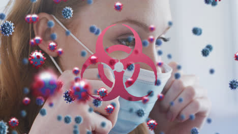 Animation-of-virus-cells-and-biohazard-symbol-over-caucasian-woman-with-face-mask