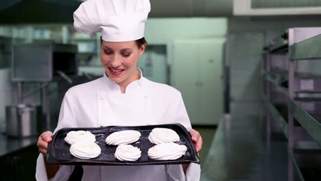 Happy-chef-smiling-at-camera-showing-tray-of-meringues