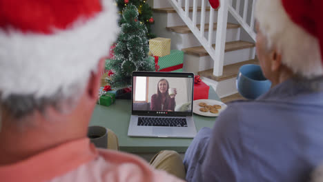 Happy-caucasian-senior-couple-on-laptop-video-call-with-female-friend-at-christmas-time