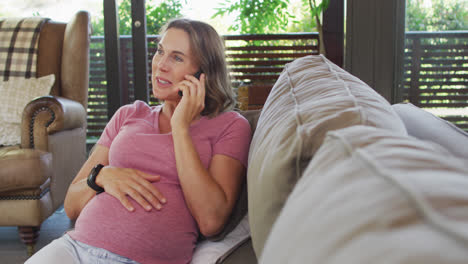 Happy-caucasian-pregnant-woman-sitting-on-sofa-and-having-phone-call