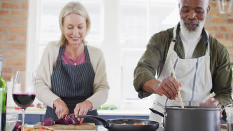 Una-Pareja-De-Ancianos-De-Raza-Mixta-Usando-Delantales-Cocinando-Juntos-En-La-Cocina-De-Casa