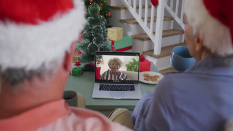 Happy-caucasian-senior-couple-on-laptop-video-call-with-senior-female-friend-at-christmas-time