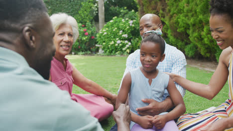 Happy-african-american-family-sitting,-talking-and-playing-in-garden