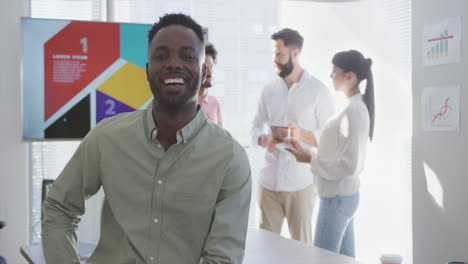 Portrait-of-happy-african-american-businessman-over-diverse-colleagues-in-office