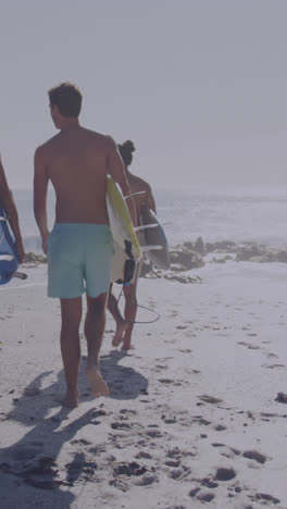 Animation-of-american-flag-over-diverse-group-of-friends-walking-with-surfboards-at-beach