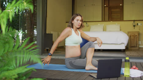 Caucasian-pregnant-woman-practicing-yoga-at-home-with-online-lessons
