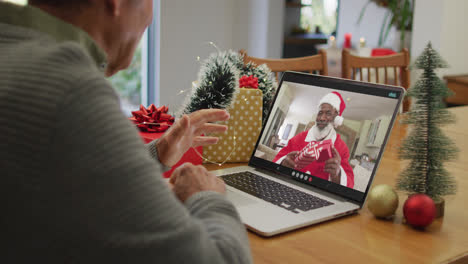 Kaukasischer-älterer-Mann-Mit-Weihnachtsvideoanruf-Auf-Dem-Laptop-Mit-Afroamerikanischem-Weihnachtsmann-Auf-Dem-Bildschirm
