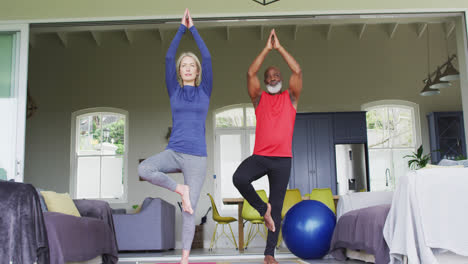 Mixed-race-senior-couple-practicing-yoga-together-at-home