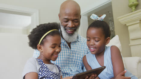Glücklicher-Afroamerikanischer-Großvater-Mit-Enkelinnen,-Die-Im-Wohnzimmer-Ein-Tablet-Benutzen