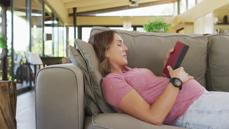 Relaxed-caucasian-pregnant-woman-lying-on-sofa-and-reading-book