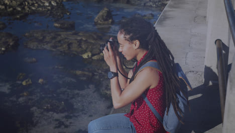 Animation-of-light-spots-over-biracial-woman-taking-photo-with-camera-on-promenade