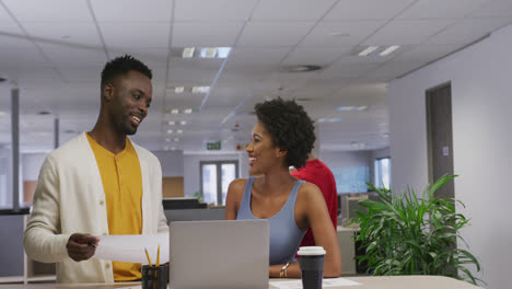 Happy-african-american-male-and-female-business-colleagues-talking-and-using-laptop