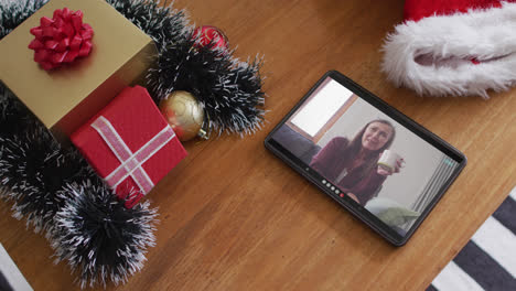 Smiling-caucasian-woman-drinking-coffee-on-christmas-video-call-on-tablet